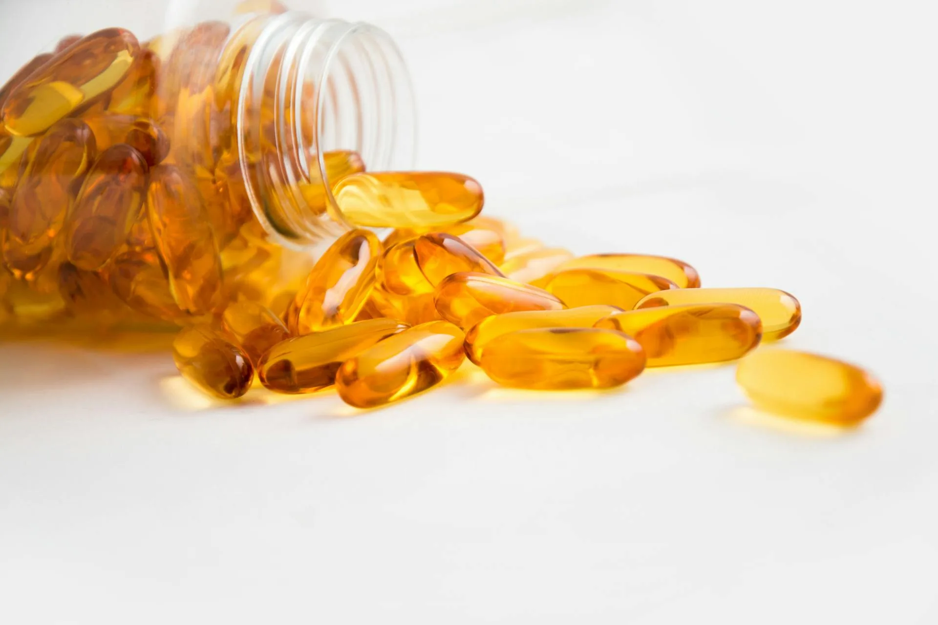 Omega-3 riebalų rūgštys : žuvų taukų kapsulės išsiliejusios iš buteliuko ant šviesaus fono