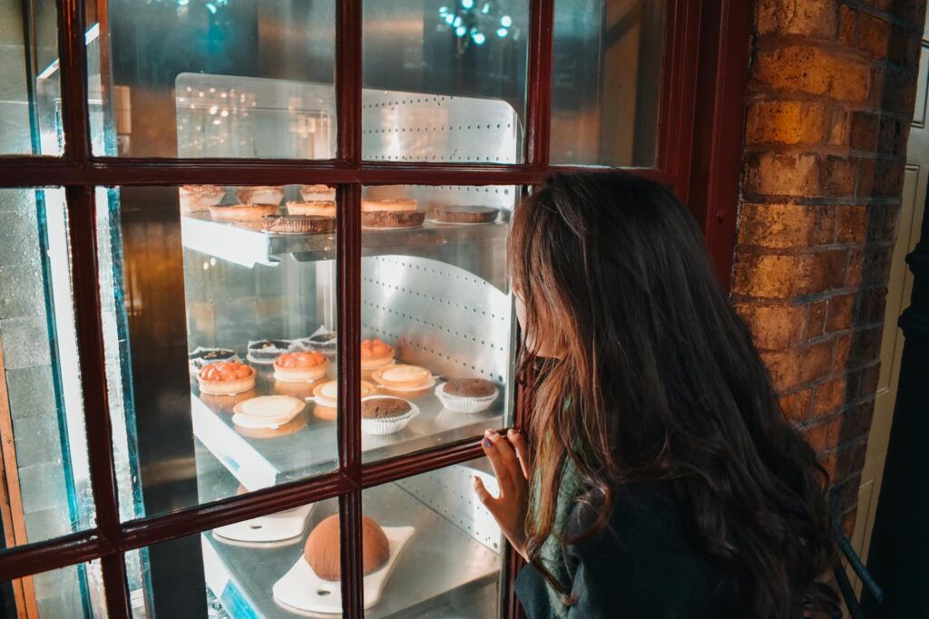 Žmogus žvelgia į desertų vitriną su pyragėliais ir keksiukais per stiklinį langą