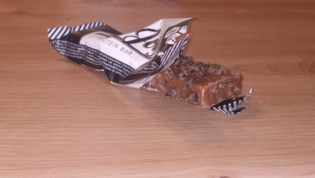 Proteino batonėlis ant medinio stalo – baltyminis batonėlis praplėštu įpakavimu kaip sveikas užkandis